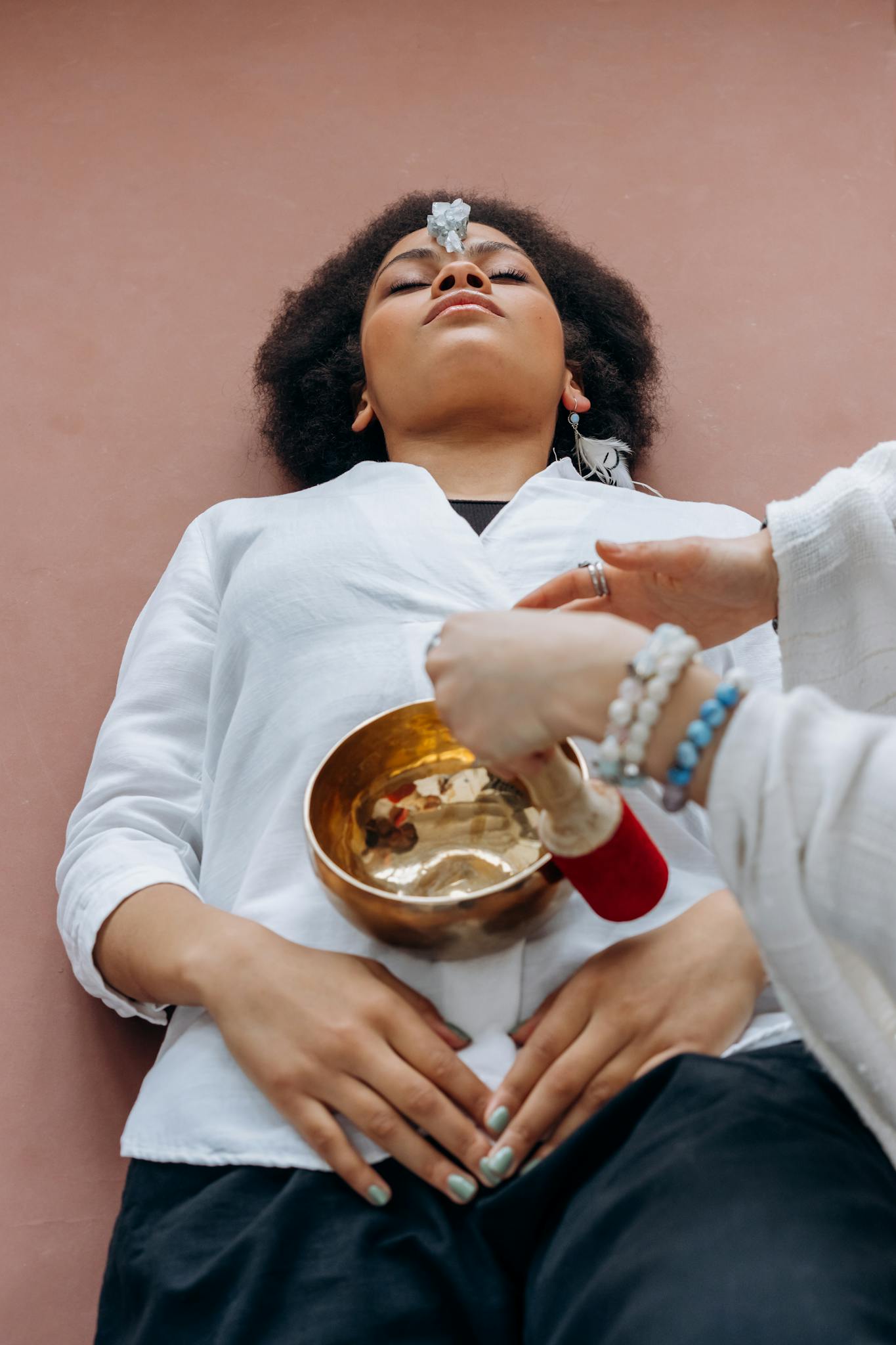 A woman experiences crystal healing therapy with a singing bowl in a serene setting.