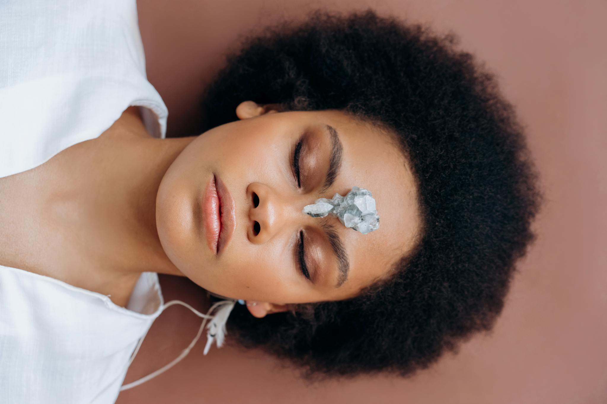 Woman practicing meditation with healing crystal on forehead, promoting wellness and relaxation.